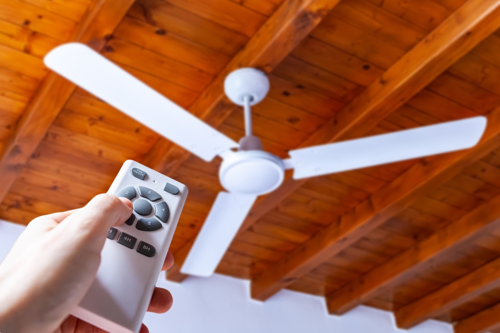 Man points a remote control at a white, ceiling mounted fan